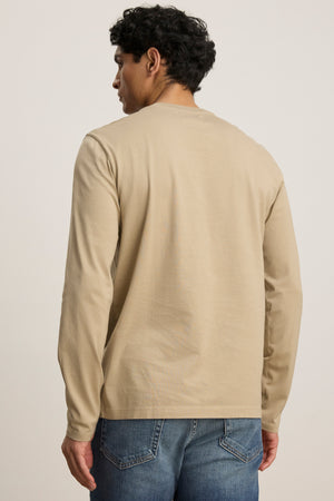 A person wearing the ALFIE TEE in beige, a midweight mercerized cotton long sleeve by Velvet by Graham & Spencer, and blue jeans stands with their back to the camera against a plain background.