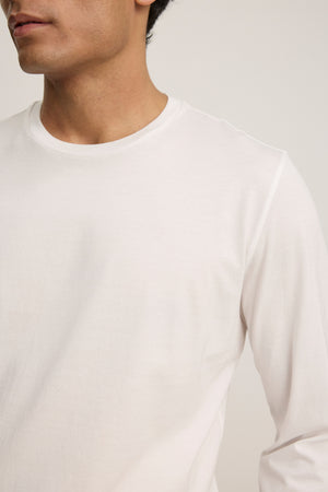 A person is shown from shoulders to mid-torso wearing the ALFIE TEE by Velvet by Graham & Spencer—a tailored fit, plain white long sleeve shirt—set against a neutral background.