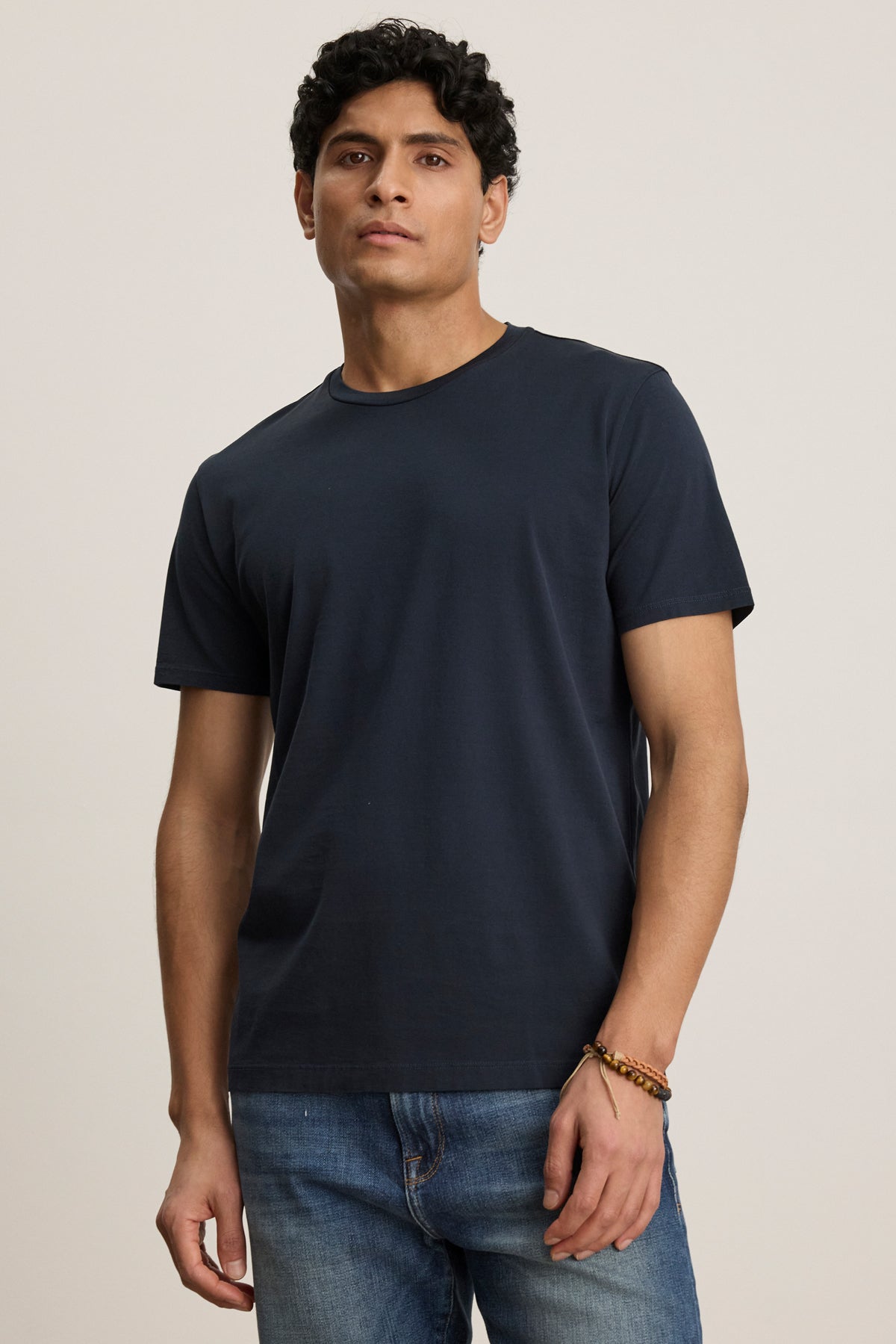 A man stands facing forward in the FRANKIE TEE by Velvet by Graham & Spencer—a plain navy blue crew neck t-shirt—paired with blue jeans against a neutral background.-39450522288321