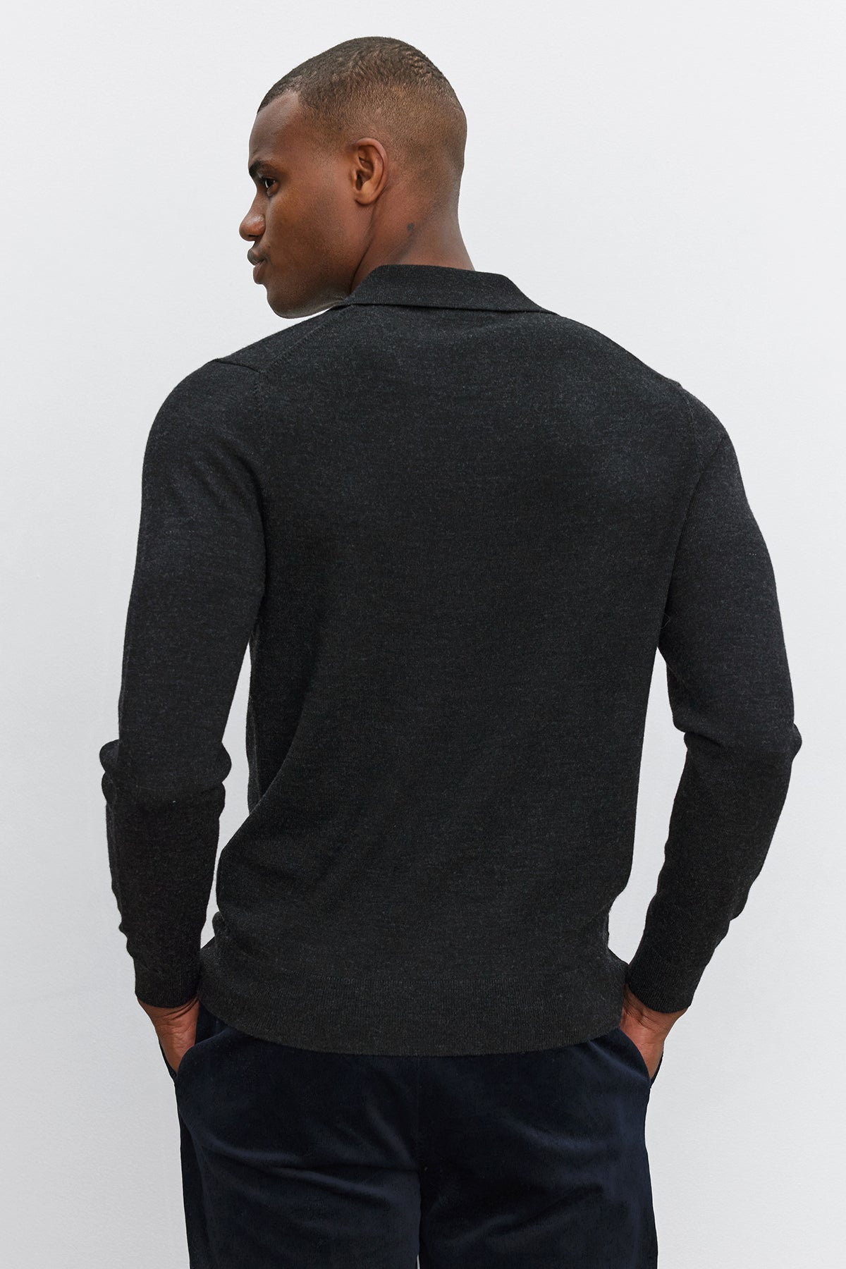   A man with short hair is wearing the ARTHUR SWEATER POLO from Velvet by Graham & Spencer and dark pants, facing away from the camera against a plain white background. 