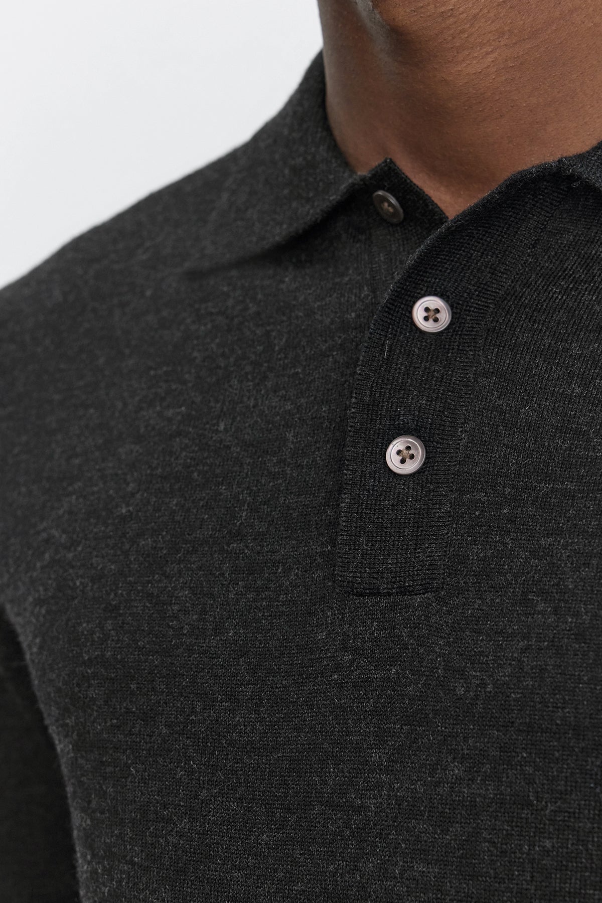   Close-up of a person wearing the ARTHUR SWEATER POLO from Velvet by Graham & Spencer. This dark grey merino wool collared shirt features a three-button placket, with the top button unfastened, showcasing its classic design. 