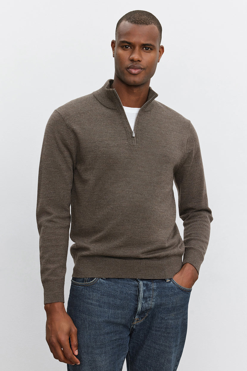 A person wearing the FLETCHER QUARTER-ZIP SWEATER by Velvet by Graham & Spencer in brown, paired with blue jeans, stands against a plain white background.