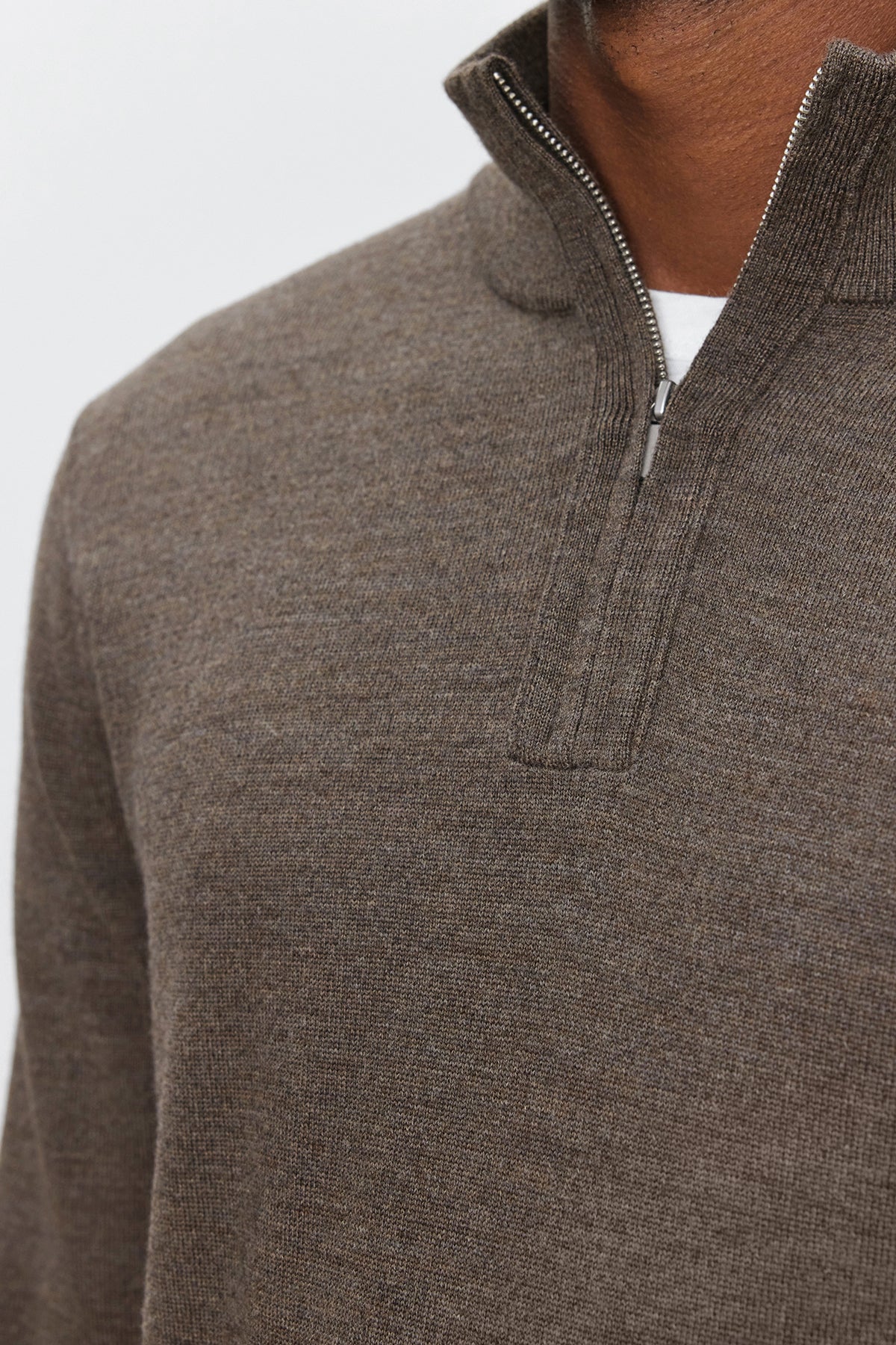   Close-up of a person wearing the FLETCHER QUARTER-ZIP SWEATER by Velvet by Graham & Spencer in brown merino wool, revealing a white shirt underneath. The background is plain and light-colored. 