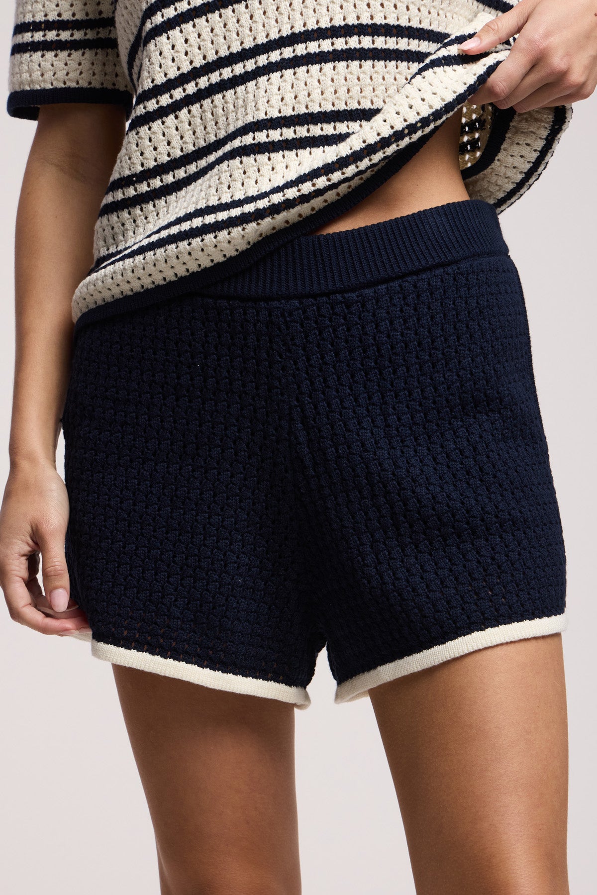 A person wearing Velvet by Graham & Spencer's JENIFER SHORT—navy lounge shorts with cream trim and an elastic waist—paired with a cream and navy striped knit top, stands against a plain background.