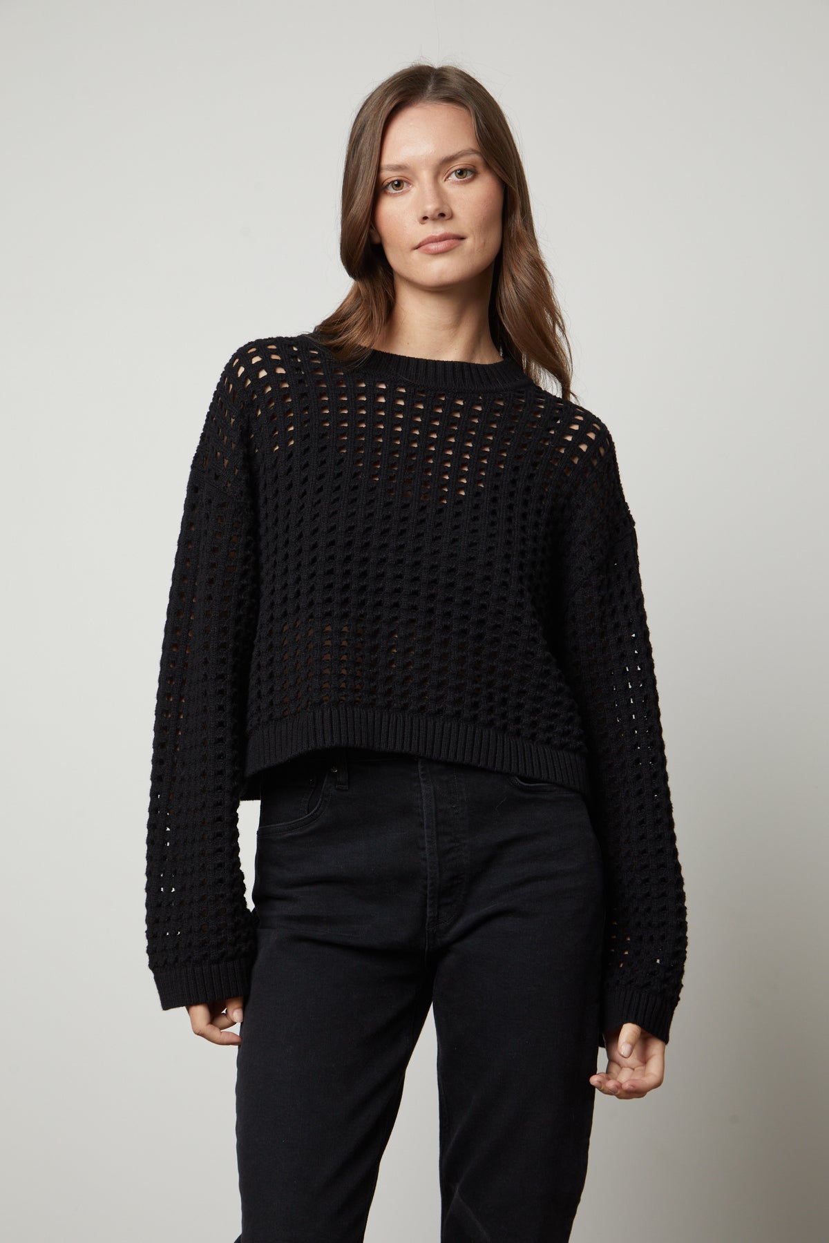   A model wearing a black SAMMIE MESH KNIT CREW NECK SWEATER by Velvet by Graham & Spencer and jeans. 