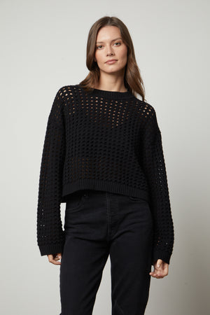 A model wearing a black SAMMIE MESH KNIT CREW NECK SWEATER by Velvet by Graham & Spencer and jeans.