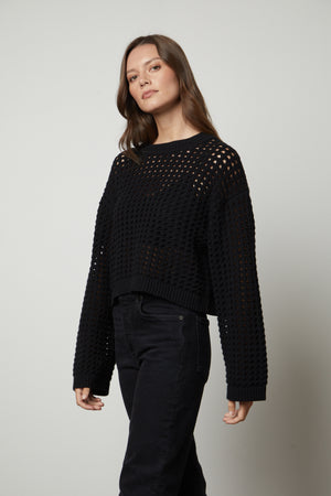 A model wearing a black SAMMIE MESH KNIT CREW NECK SWEATER by Velvet by Graham & Spencer and jeans.