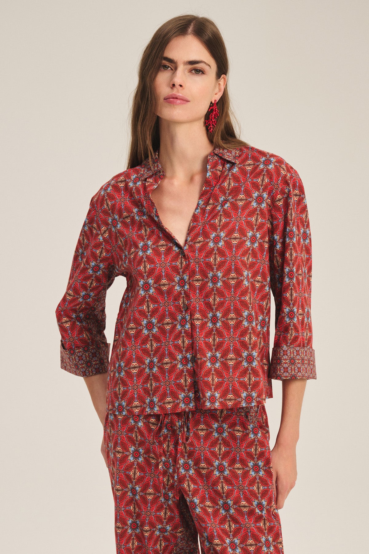 A woman wears the Velvet by Graham & Spencer MICAH SHIRT, a red patterned button-up pajama top with matching long pants, standing against a plain background.-41436010578113