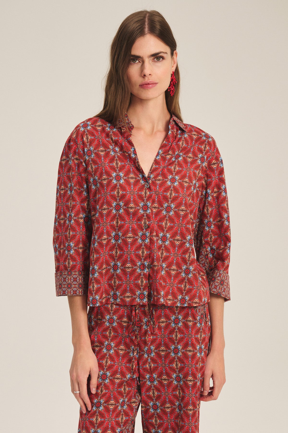 A woman wears the Velvet by Graham & Spencer MICAH SHIRT, a red patterned long-sleeve top with matching pants, standing against a plain light background.