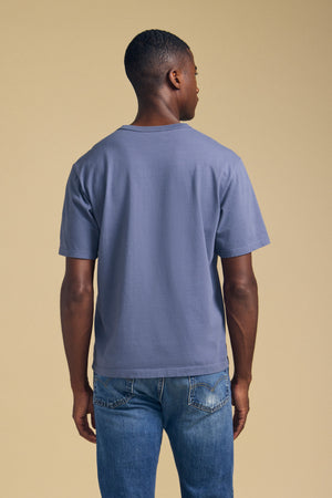 Back view of the blue WELLS short sleeve crew neck tee showcasing its relaxed fit against a beige background