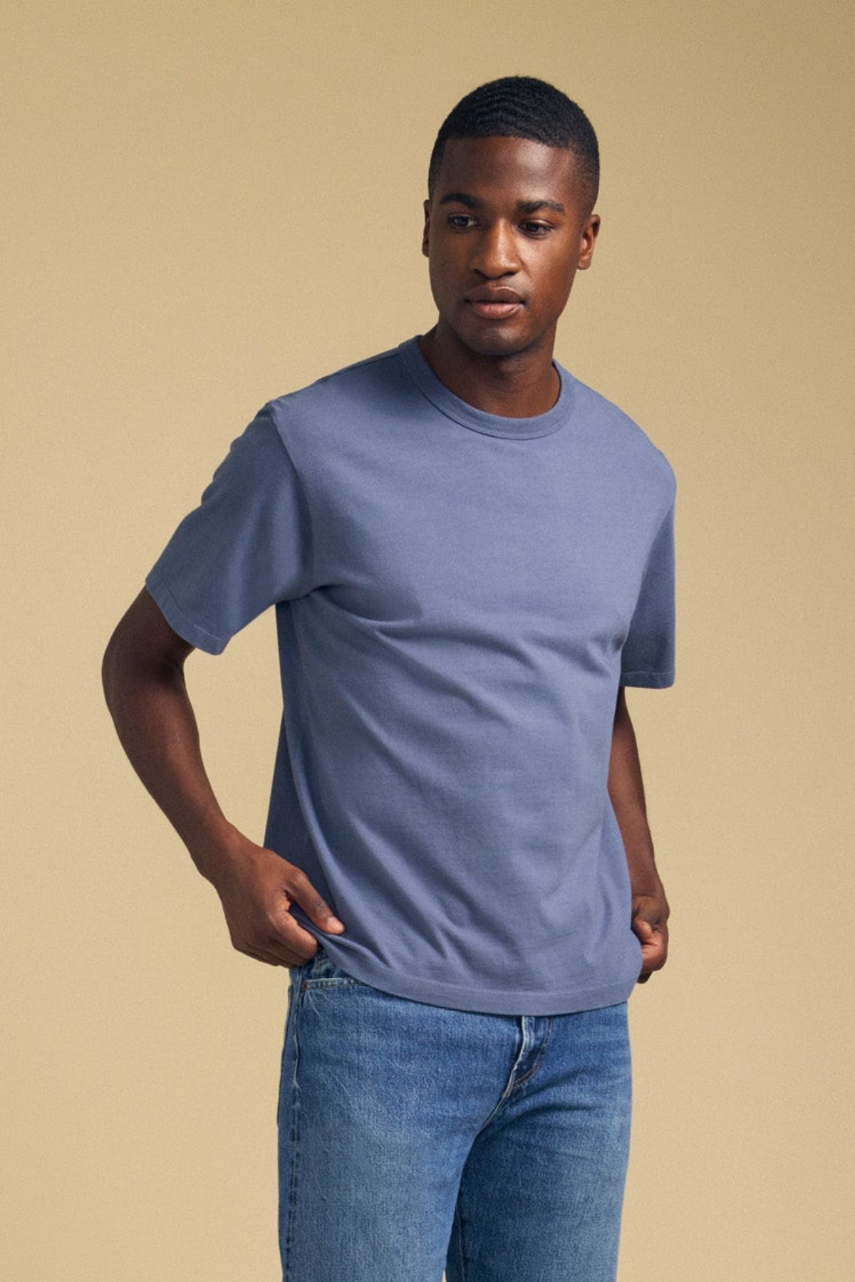 Three-quarter view of blue WELLS short-sleeve tee showcasing relaxed fit against a beige background