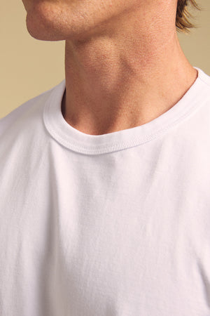 A close-up of a person's neck and shoulder wearing the WELLS TEE by Velvet by Graham & Spencer, a relaxed fit tee crafted from plain white Pima cotton, set against a neutral background.