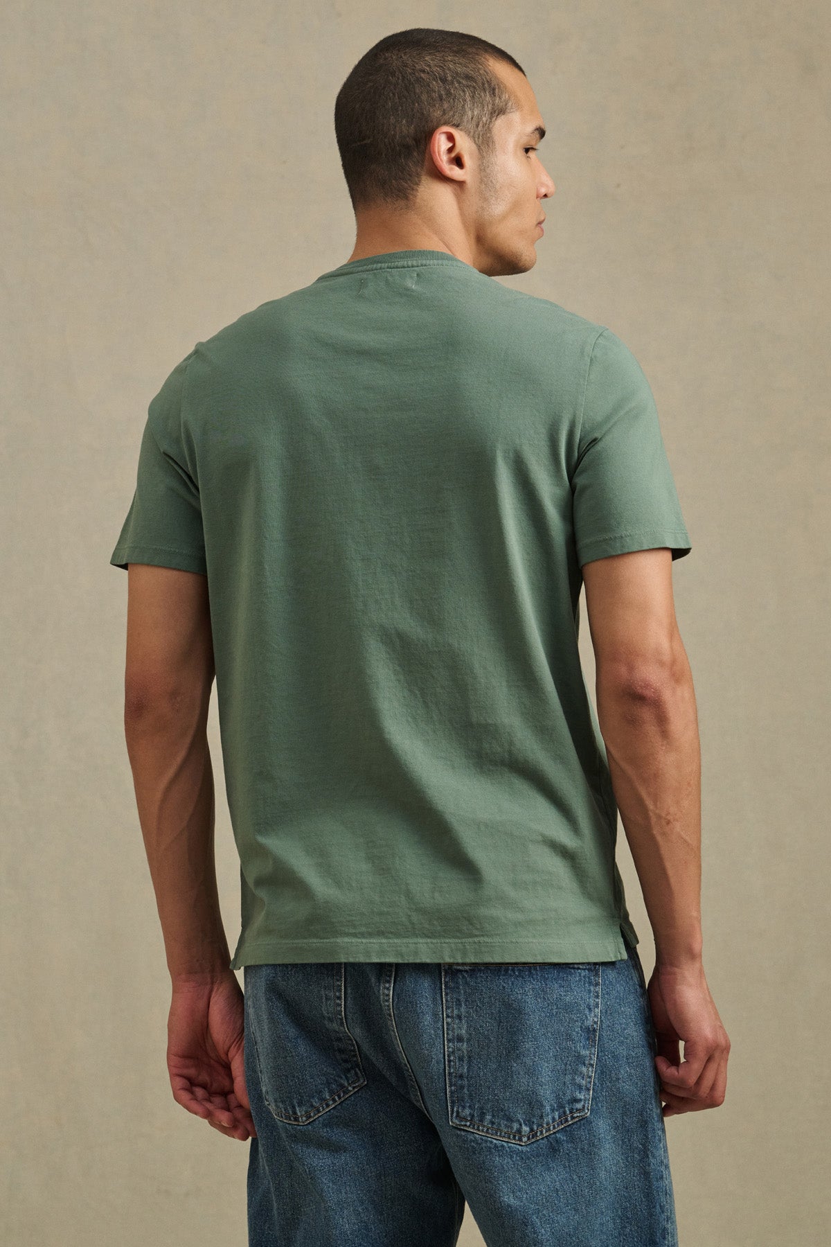 A man wearing the FELIX HENLEY by Velvet by Graham & Spencer in green and blue jeans stands with his back to the camera against a neutral background.-41479917207745