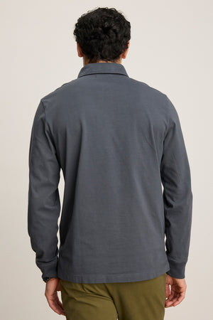 A man, seen from behind against a plain background, wears the FLINT POLO by Velvet by Graham & Spencer—a long-sleeved dark gray shirt with ribbed cuffs—paired with olive green pants.