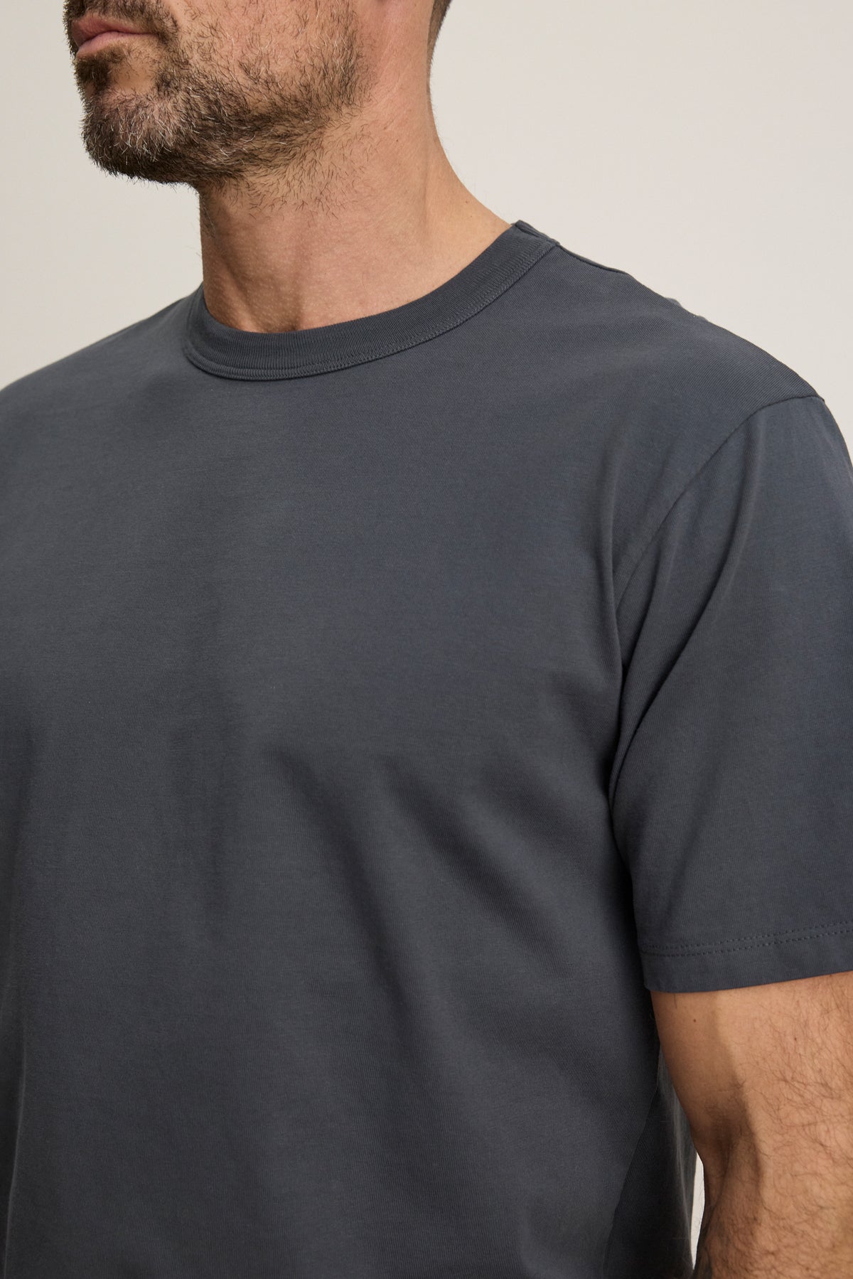 A man with a short beard is wearing the WELLS TEE by Velvet by Graham & Spencer, a relaxed fit dark gray crew neck t-shirt. The image is cropped from his shoulders to just above his mouth.-39680486211777