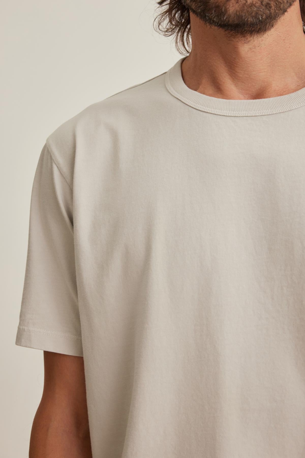 A person wearing the WELLS TEE by Velvet by Graham & Spencer, a plain light-colored shirt cropped at the shoulders and neck, standing against a neutral background.-38643375669441