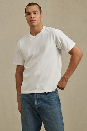 A man poses against a neutral background wearing the WELLS TEE by Velvet by Graham & Spencer, a relaxed fit in plain white Pima cotton jersey, paired with blue jeans—perfect for all-day comfort.