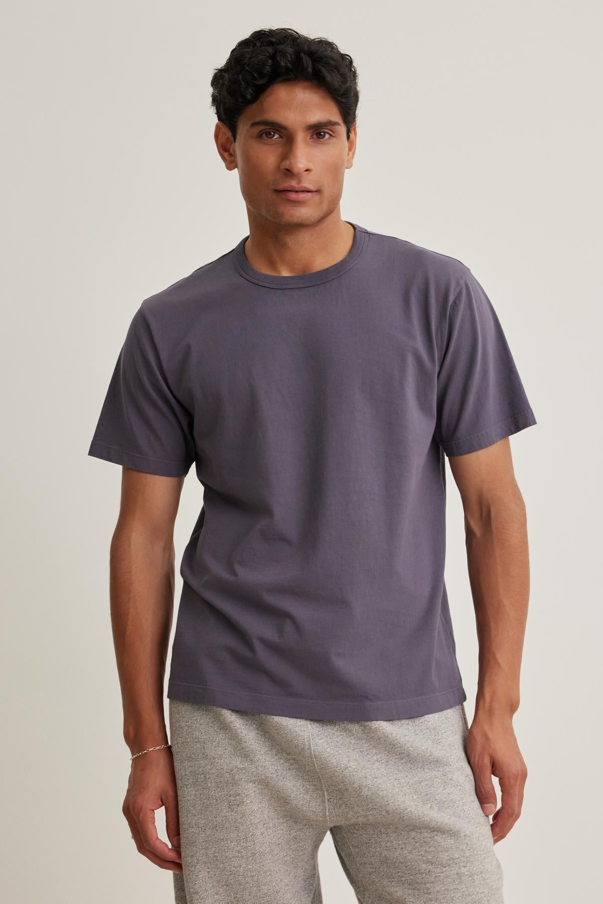   A man wearing the WELLS TEE by Velvet by Graham & Spencer and light gray pants stands against a neutral background. 