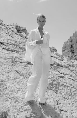 Description: A woman in a white suit, wearing Velvet by Jenny Graham's PICO PANT, soft linen pants with an elastic waistband, standing on a rock.