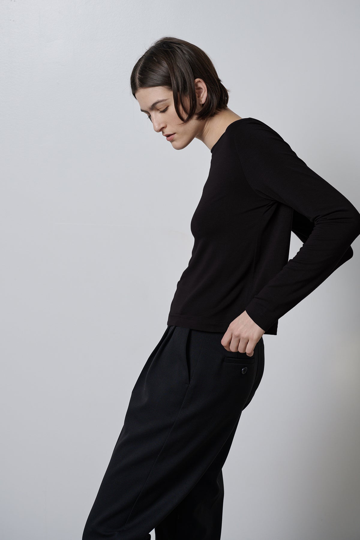   A woman wearing black trousers and a black long-sleeved top, the Velvet by Jenny Graham PACIFICA TEE in a soft hand rib knit fabric. 