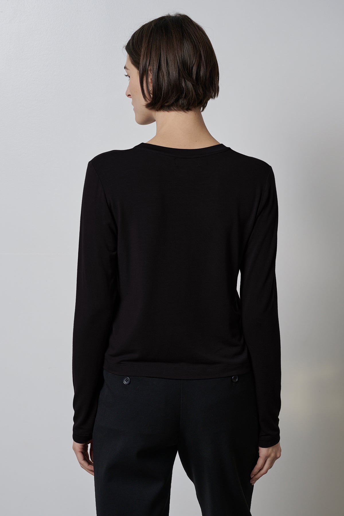 A woman wearing a black rib knit PACIFICA TEE by Velvet by Jenny Graham and slim-fitting black pants is seen from the back view.-35416710152385