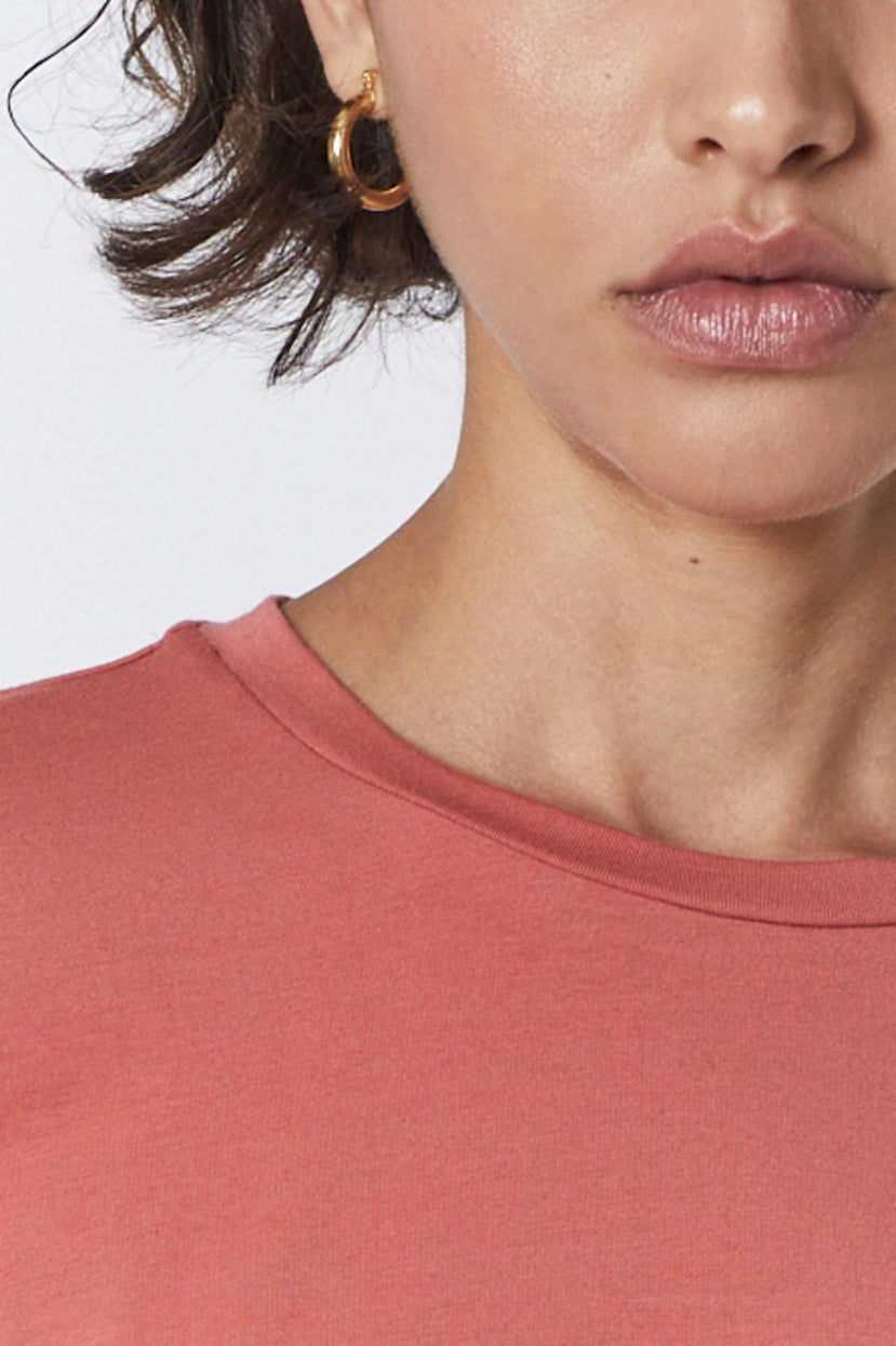 A woman wearing a pink Velvet by Jenny Graham rib knit Pacifica Tee with gold hoop earrings.