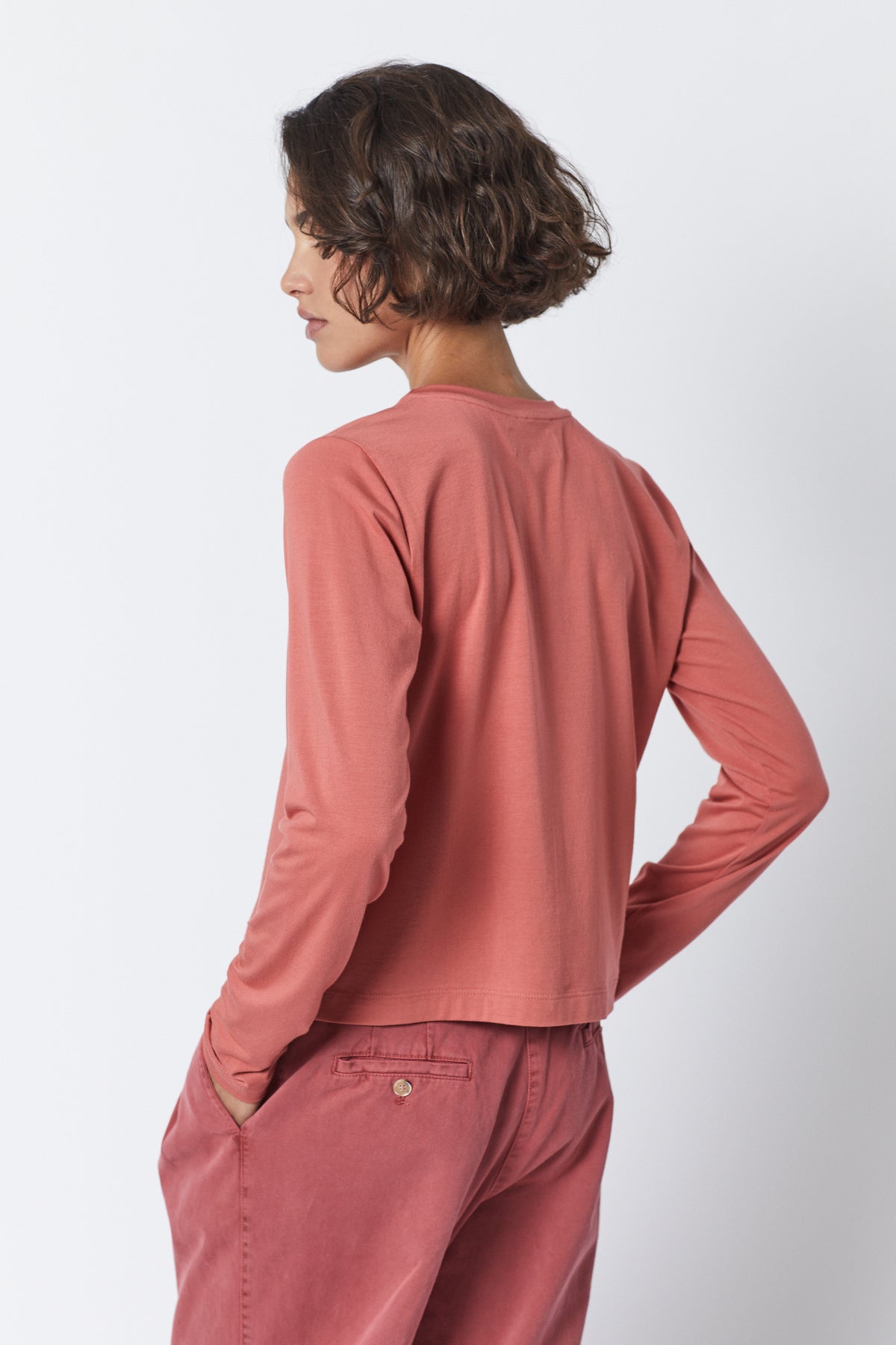   The back view of a woman wearing pink pants and a long-sleeved Velvet by Jenny Graham PACIFICA TEE made from rib knit fabric. 