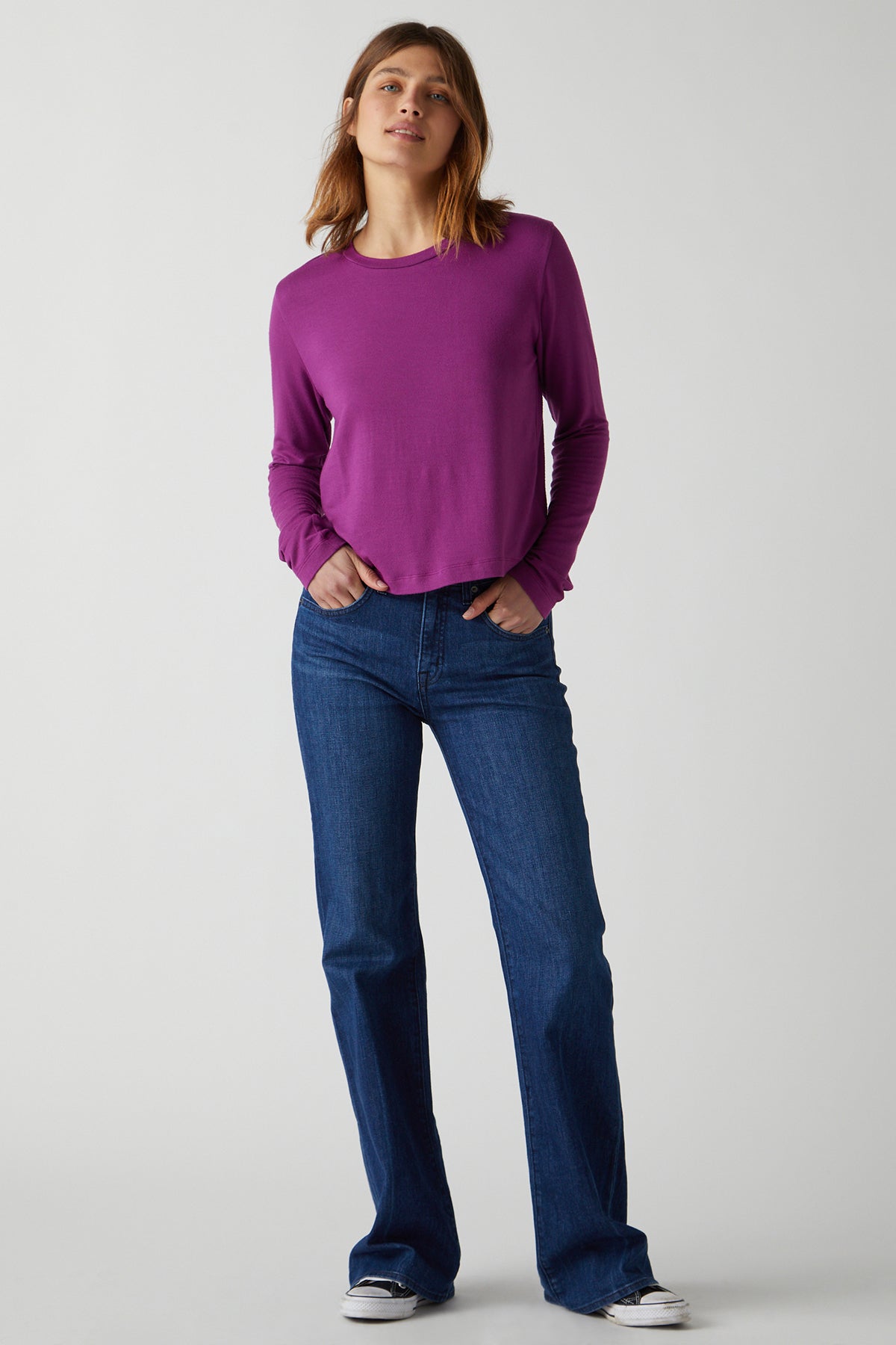   A woman wearing a Pacifica Tee by Velvet by Jenny Graham, a rib knit long-sleeved top in purple, and slim-fit blue jeans. 