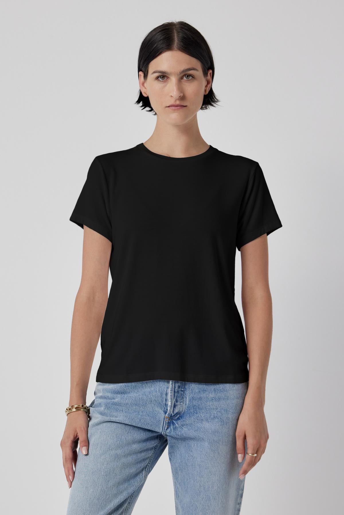   Woman in a classic Velvet by Jenny Graham SOLANA TEE and blue jeans standing against a plain background. 