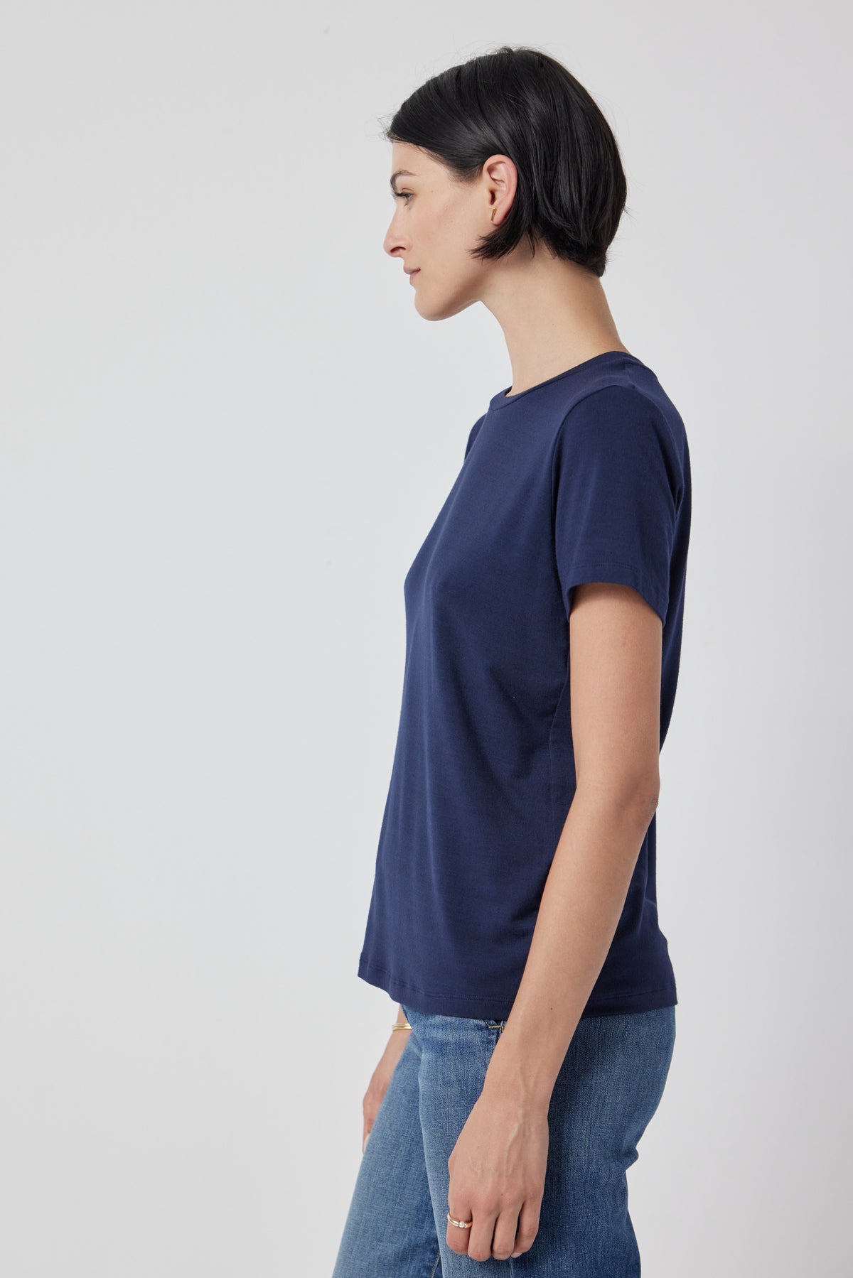   Profile view of a woman wearing a navy blue Velvet by Jenny Graham Solana Tee and jeans against a white background. 