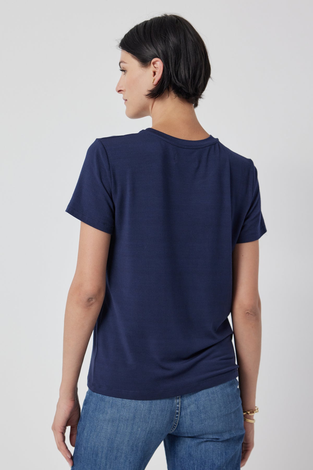   Woman posing with her back turned to the camera, wearing a navy blue Velvet by Jenny Graham SOLANA TEE and jeans. 