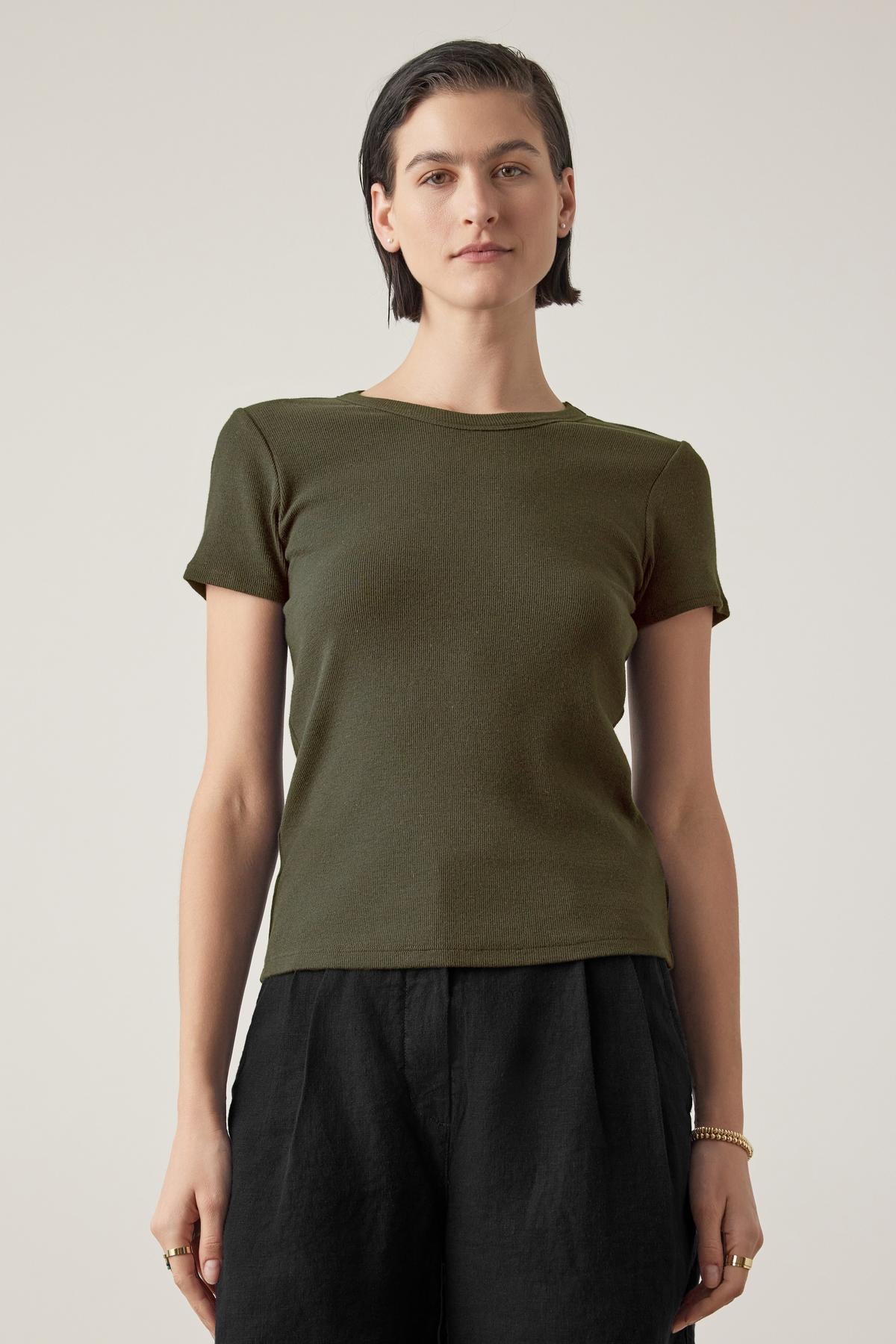   Person with short dark hair wearing a fitted silhouette dark green short-sleeve BEDFORD TEE by Velvet by Jenny Graham and black pants, standing against a plain background. 