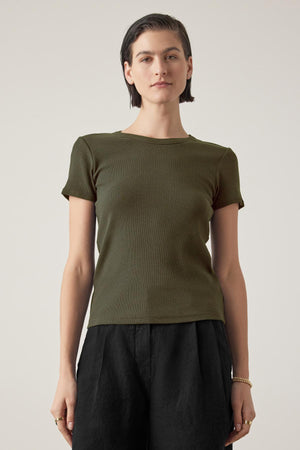 Person with short dark hair wearing a fitted silhouette dark green short-sleeve BEDFORD TEE by Velvet by Jenny Graham and black pants, standing against a plain background.