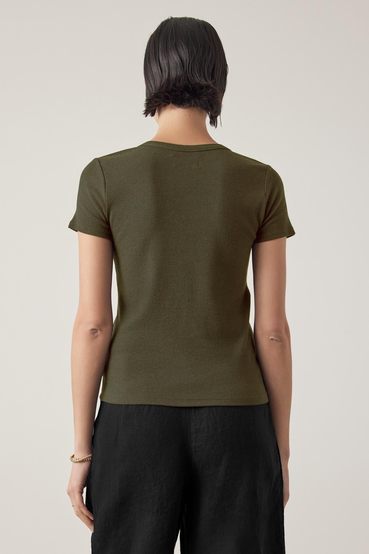   A person wearing a short-sleeved, fitted silhouette olive green BEDFORD TEE by Velvet by Jenny Graham and black pants is seen from the back against a plain background. 