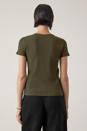 A person wearing a short-sleeved, fitted silhouette olive green BEDFORD TEE by Velvet by Jenny Graham and black pants is seen from the back against a plain background.