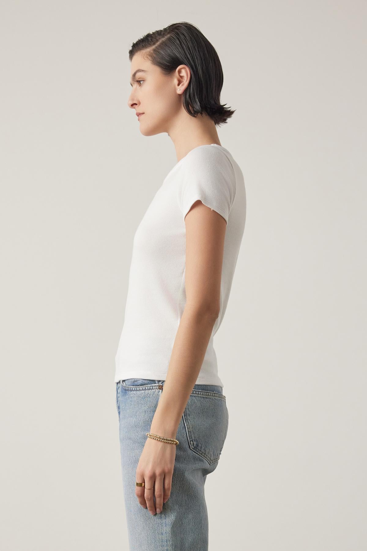   Side profile of a woman with short hair wearing a white BEDFORD TEE by Velvet by Jenny Graham with a crew neckline and jeans, standing against a light backdrop. 