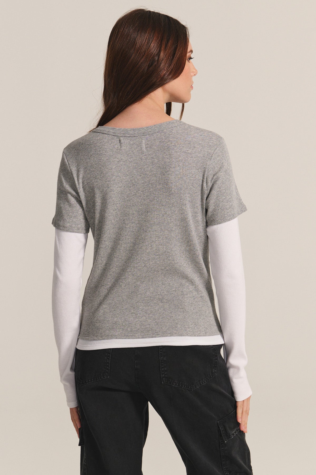 Model stands with back to camera, wearing the BRONSON TEE by Velvet by Graham & Spencer—a gray modal rib crewneck layered over a white long-sleeve shirt and paired with black pants.-40334122385601