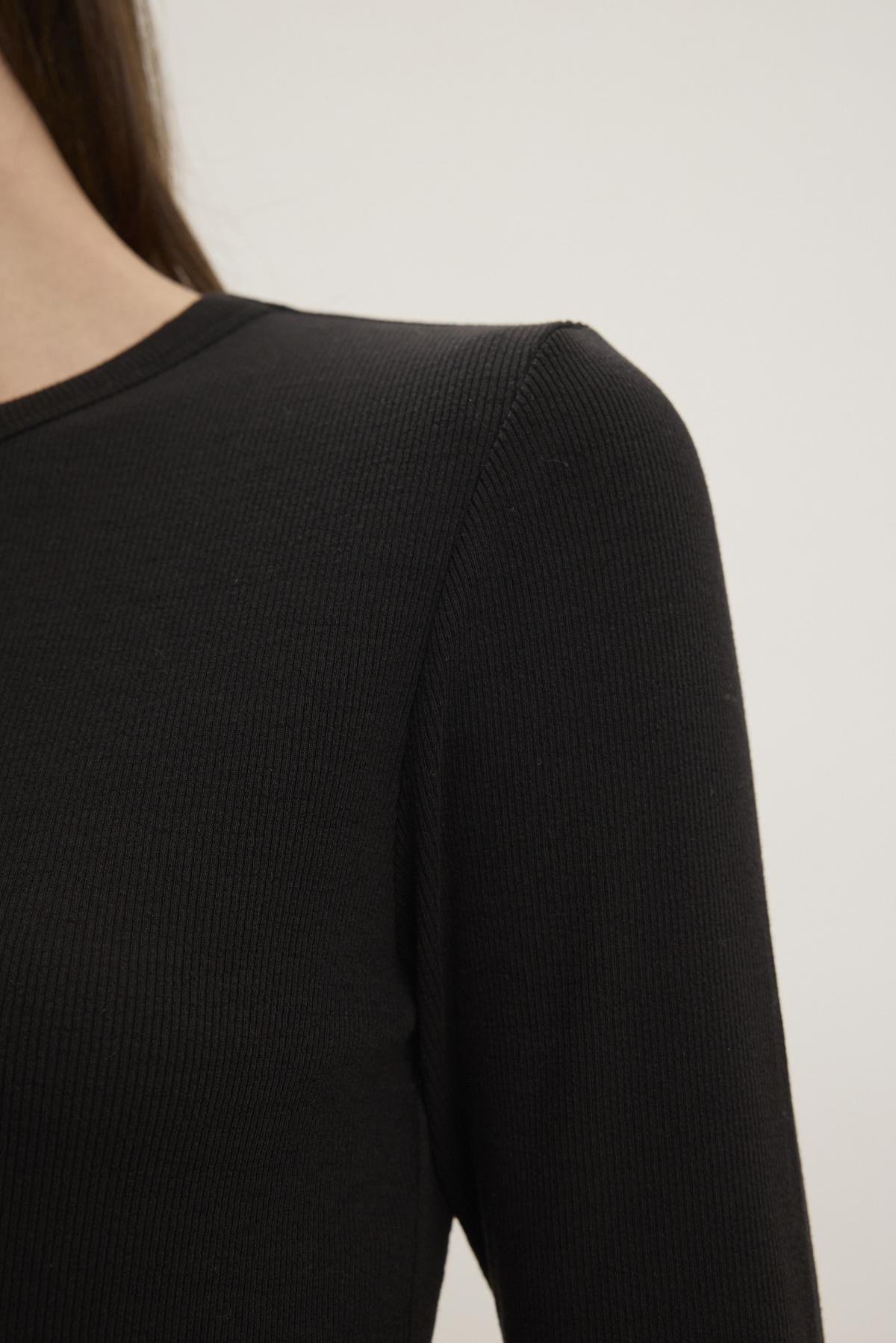 A close-up of a person wearing the Velvet by Jenny Graham CAMINO TEE, showcasing its sleek black modal rib material on the shoulder and part of the arm against a plain background. The slimmer fit enhances its timeless appeal.-38352888856769