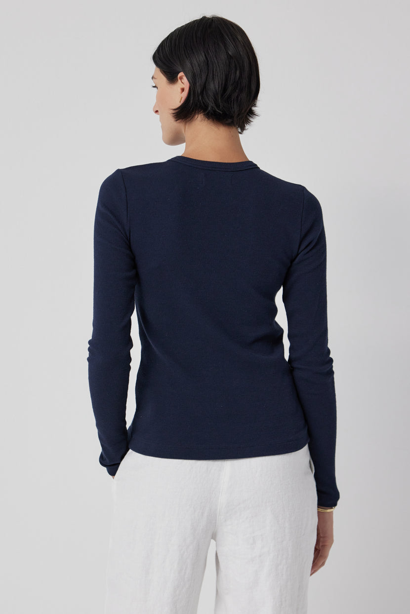 A woman seen from behind wearing a navy blue long-sleeve, slim-fit Velvet by Jenny Graham CAMINO TEE and white pants.