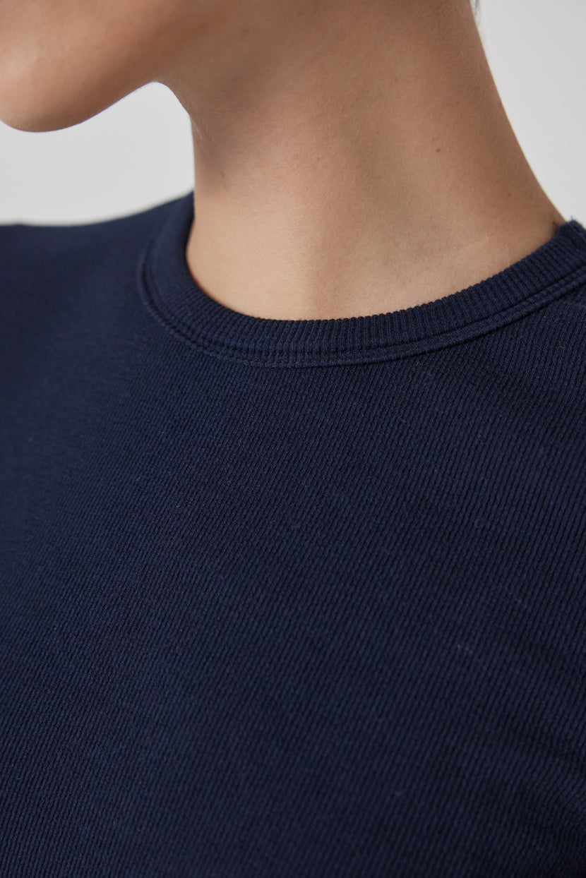Close-up of a person wearing a navy blue CAMINO TEE by Velvet by Jenny Graham with a slimmer fit and a ribbed crew neckline.