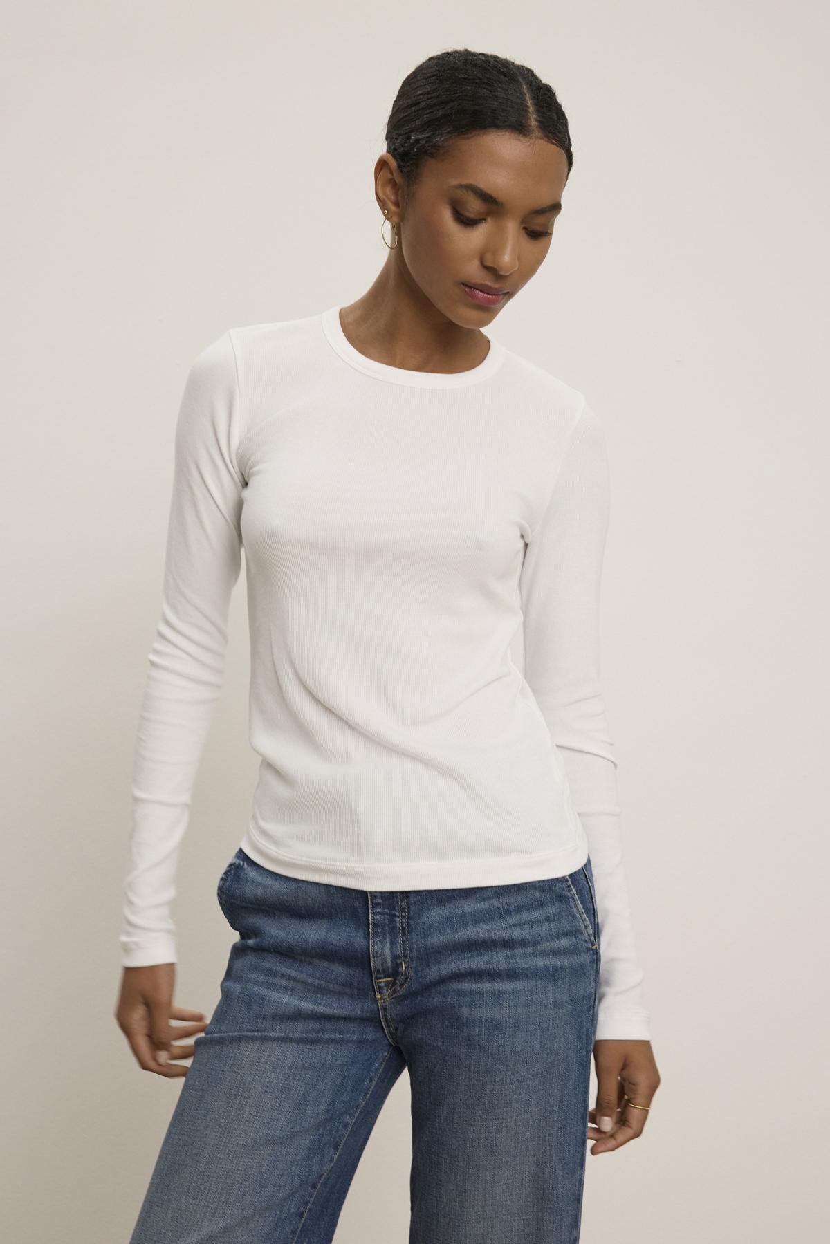 Clad in the elegant CAMINO TEE by Velvet by Jenny Graham paired with slimmer-fit blue jeans, a person stands against a plain background, showcasing a versatile style.-38352889708737