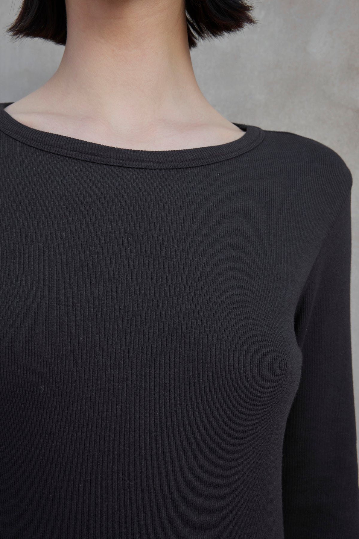   Close-up of a person wearing the Velvet by Jenny Graham CORONADO DRESS, which features long sleeves and a ribbed texture. The focus is on the upper torso, neckline, and part of the neck. The background is neutral-toned. 