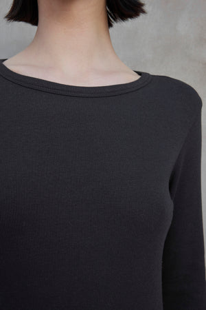 Close-up of a person wearing the Velvet by Jenny Graham CORONADO DRESS, which features long sleeves and a ribbed texture. The focus is on the upper torso, neckline, and part of the neck. The background is neutral-toned.