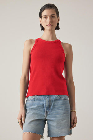 A person wearing the CRUZ TANK TOP from Velvet by Jenny Graham in a red sleeveless design, paired with denim shorts, standing against a plain background.