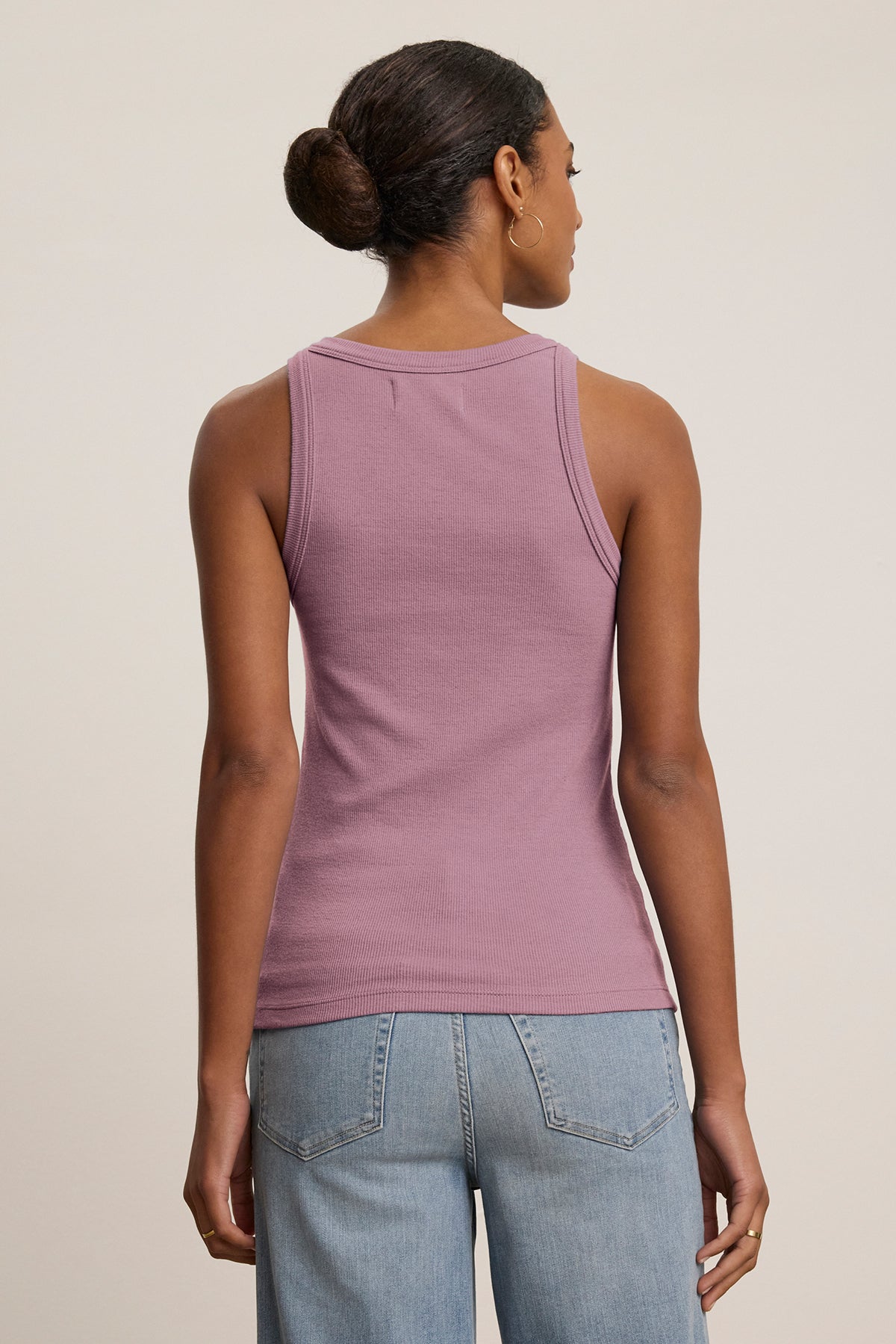 A person with their hair in a bun is wearing the Velvet by Jenny Graham CRUZ TANK TOP, a sleeveless purple ribbed cotton-modal top, paired with blue jeans, highlighting the versatility of a capsule wardrobe as they face away.-38662658883777