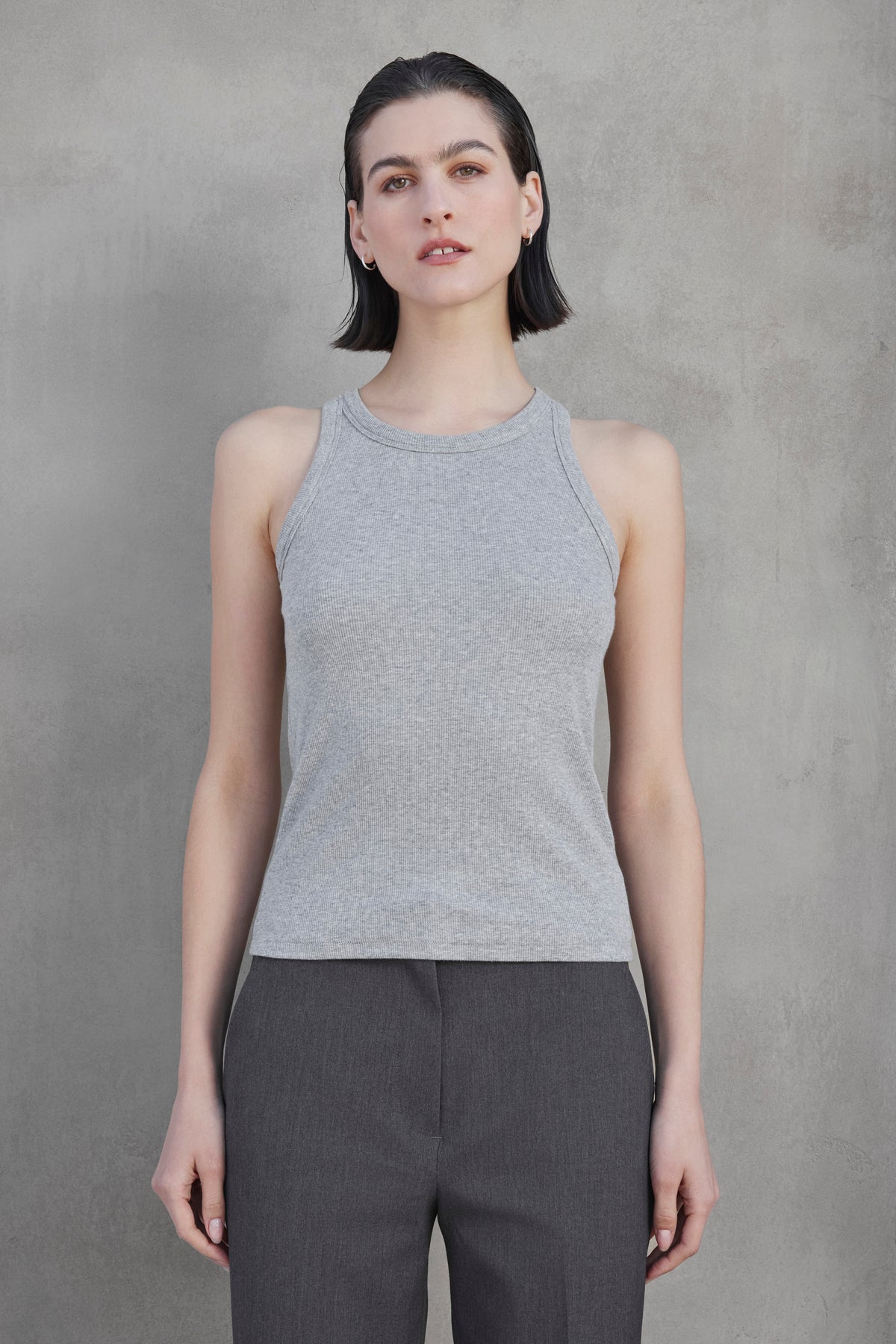 A person with short dark hair wears the versatile CRUZ TANK TOP from Velvet by Jenny Graham in a gray sleeveless top and dark gray pants, standing against a plain gray background.-37659959066817