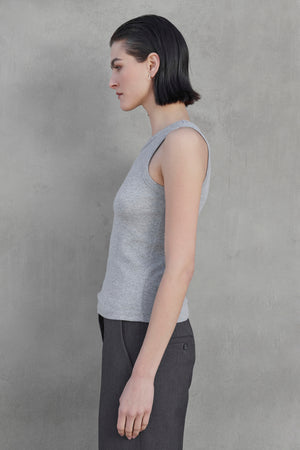 Side profile of a person with short dark hair, wearing the CRUZ TANK TOP from Velvet by Jenny Graham in a sleeveless gray ribbed cotton-modal blend shirt and dark gray pants, standing against a plain gray background.