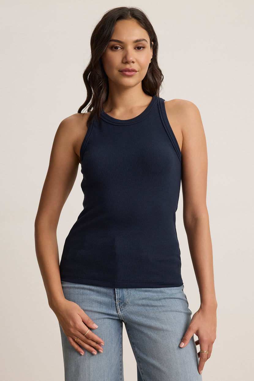 A person wearing the versatile CRUZ TANK TOP in navy by Velvet by Jenny Graham, paired with light blue jeans, stands against a plain background, exemplifying a capsule wardrobe.