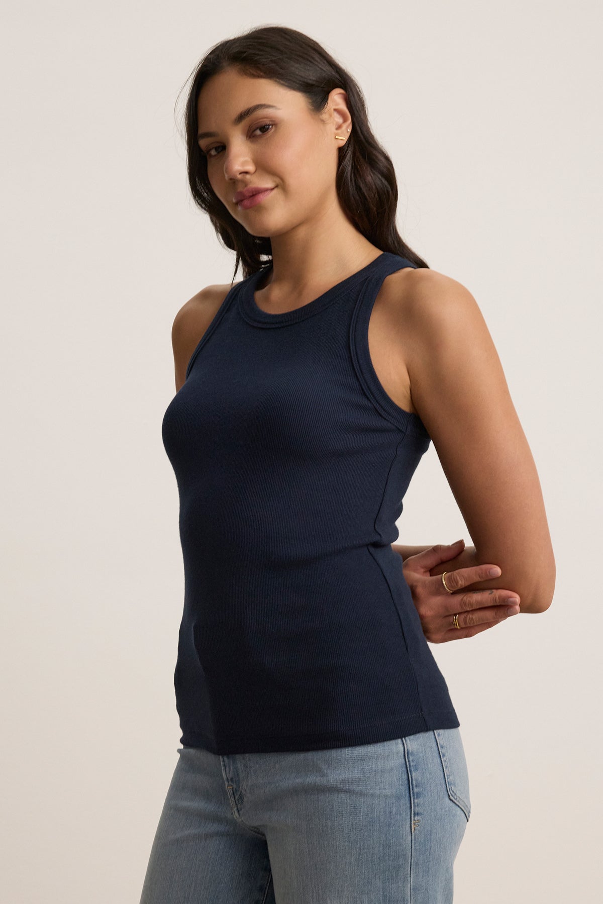   A person wearing the Velvet by Jenny Graham CRUZ TANK TOP, a sleeveless navy blue piece, paired with light jeans, stands elegantly against a neutral background—an ideal piece for any capsule wardrobe. 