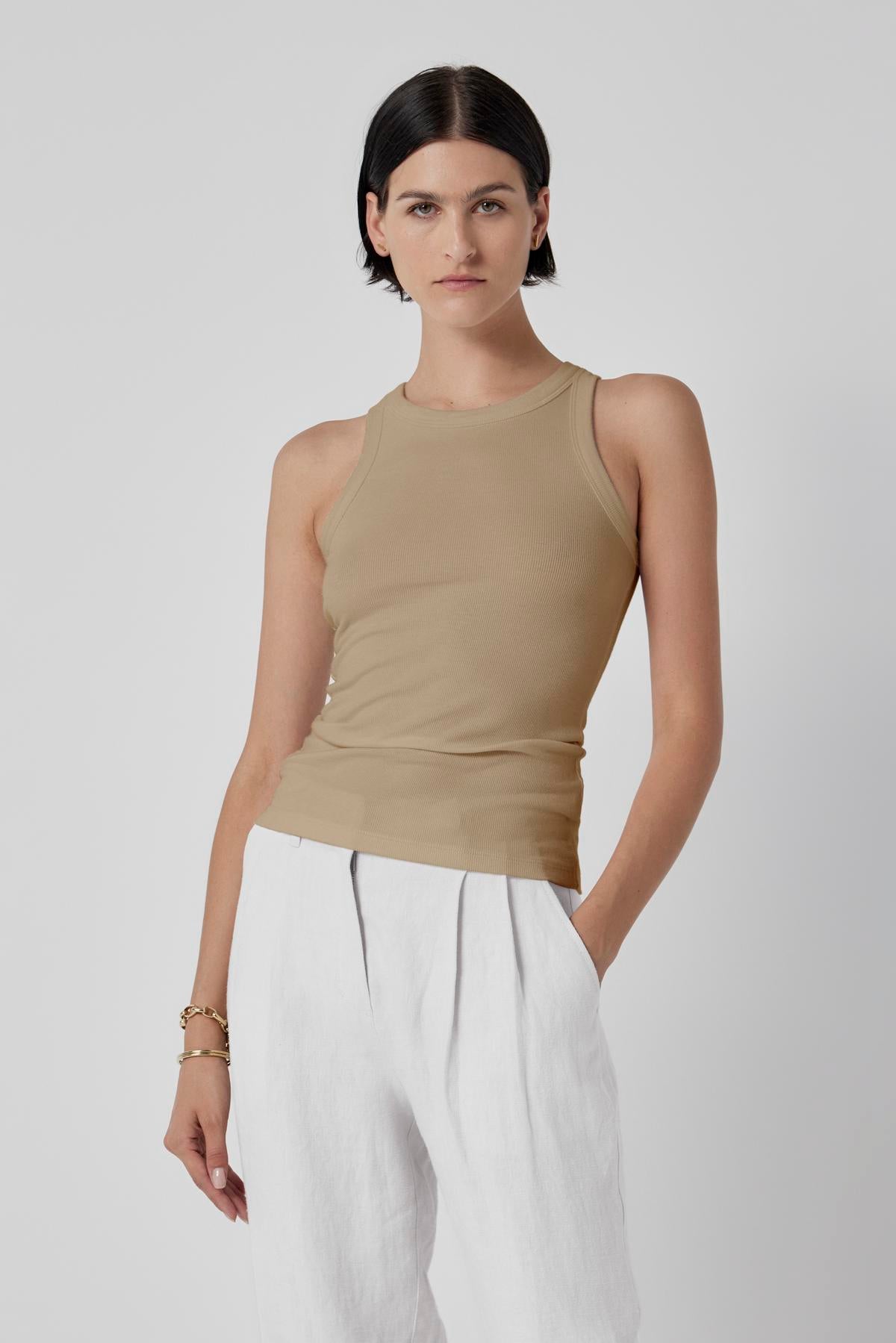   A woman in a beige Velvet by Jenny Graham Cruz tank top and chic white trousers against a light background. 